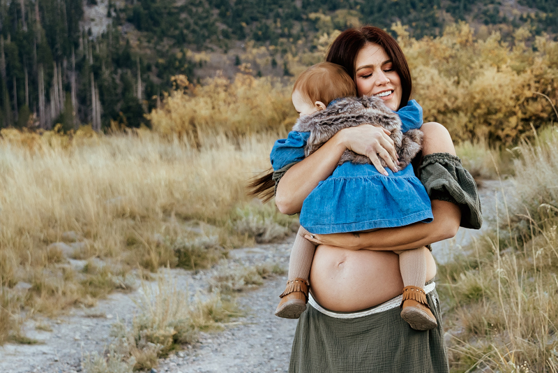 Eastern Sierras Family Photographer, Mammoth Lakes, CA, Maternity Photography, pregnant mother with bare belly holding her infant and dancing in nature